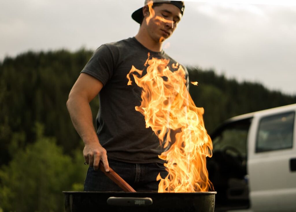 Um homem mexendo em uma churrasqueira com o fogo alto