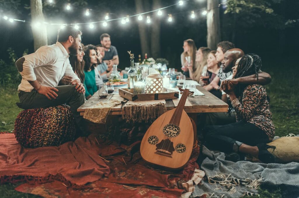 Amigos sentados em uma mesa com luzes de decoração e um violão apoiado no pé da mesa 