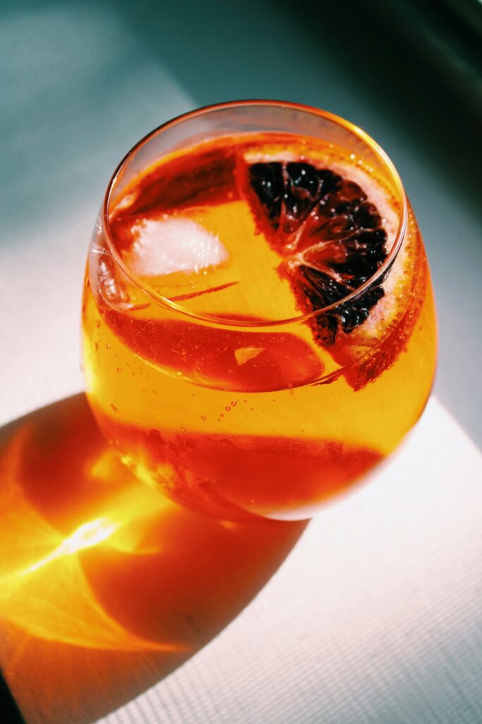 Drink aperol spritz em um copo de vidro, em cima de uma mesa branca