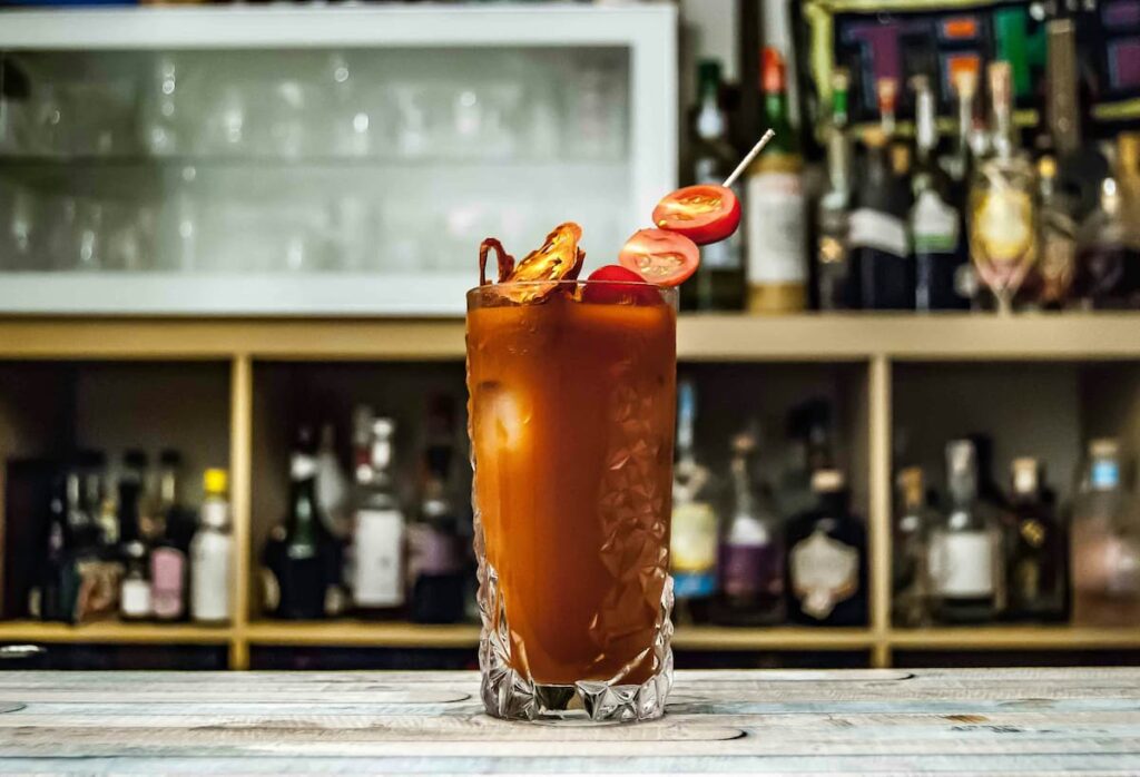 Bloody Mary em uma mesa de bar com bebidas na prateleira atrás 
