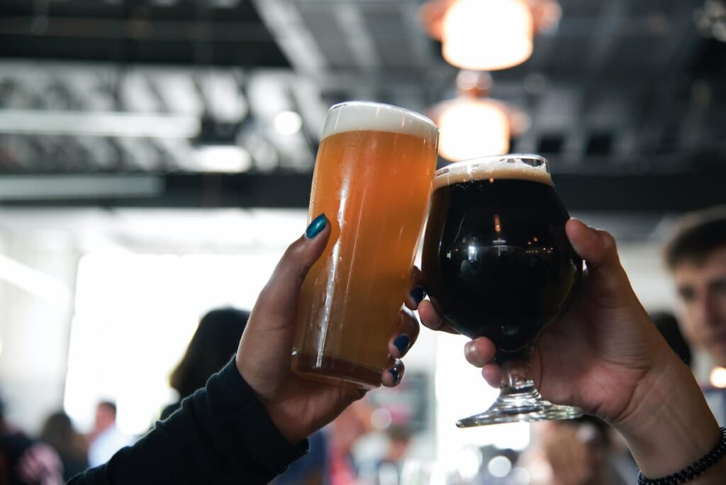 Duas pessoas brindando com cerveja, uma com cerveja clara e outra com a cerveja escura
