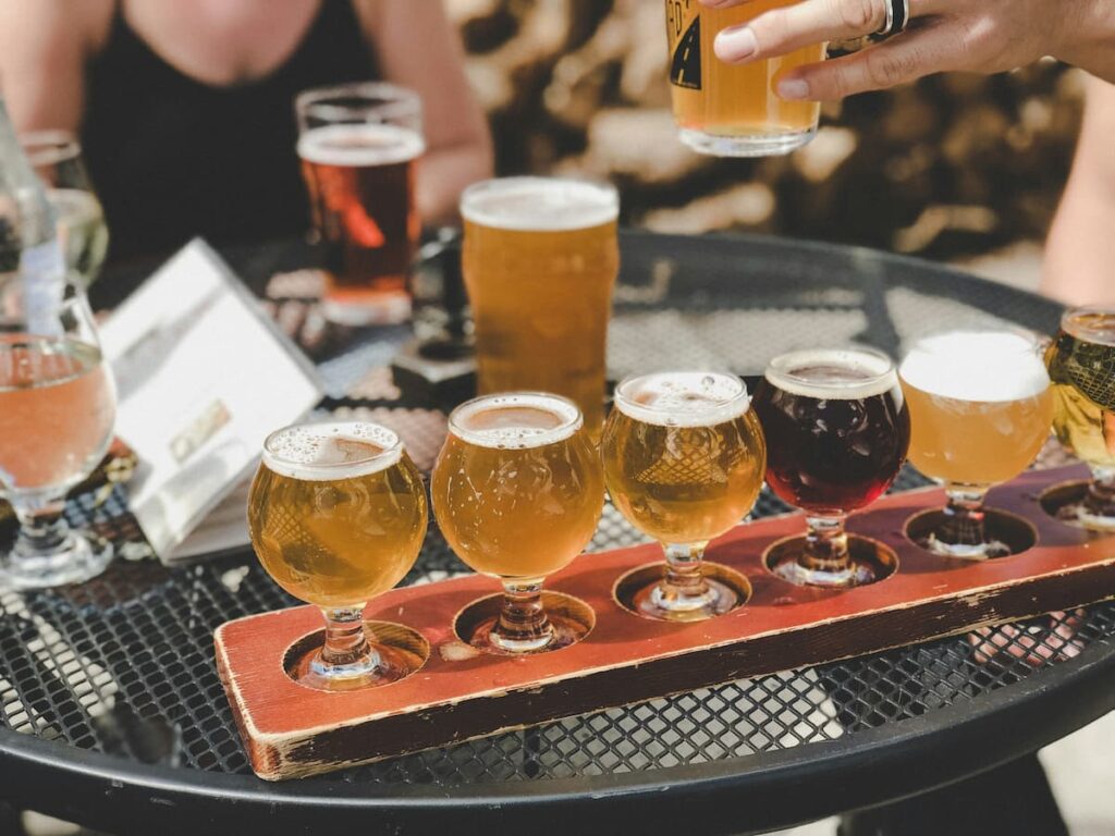 5 copos de diferentes tipos de cerveja, em uma mesa de bar