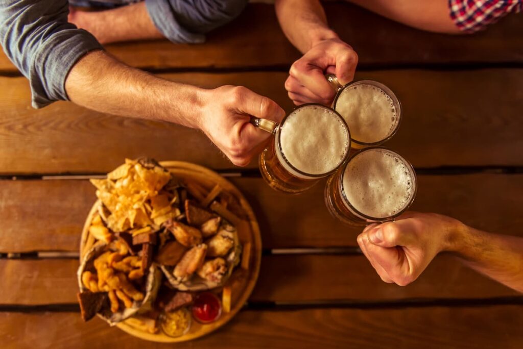 Amigos brindando com cerveja e petiscos na mesa.