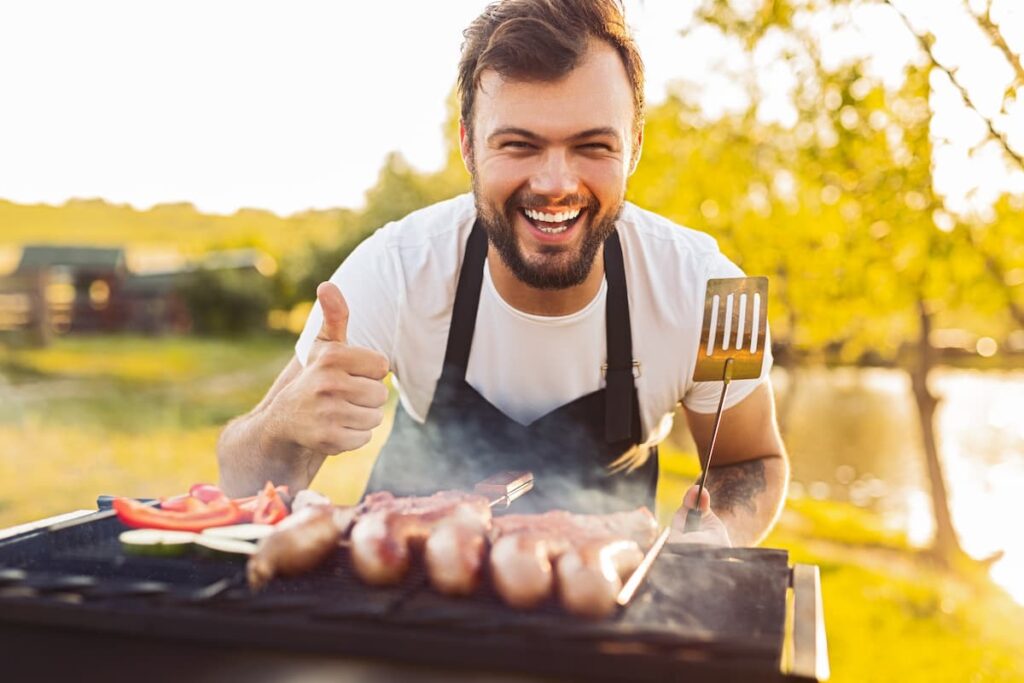 Um homem na frente de uma churrasqueira sorrindo para a foto