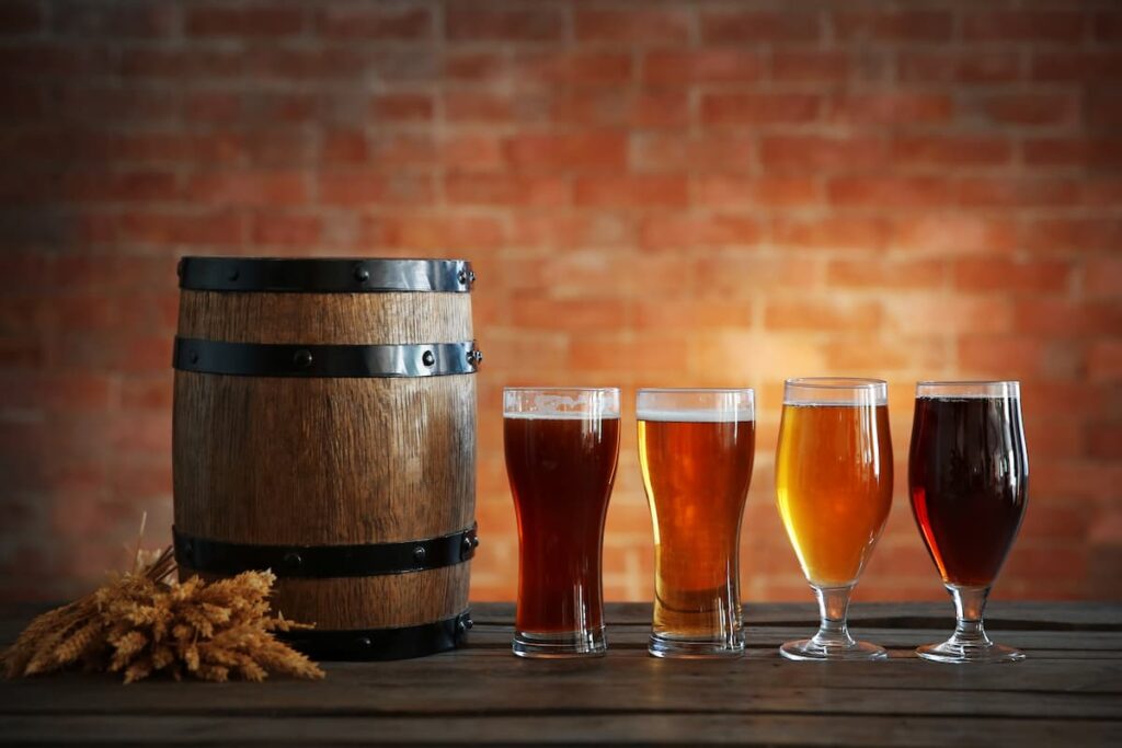 Um barril de madeira e ao lado dele, 4 copos de cerveja com diferentes tonalidades
