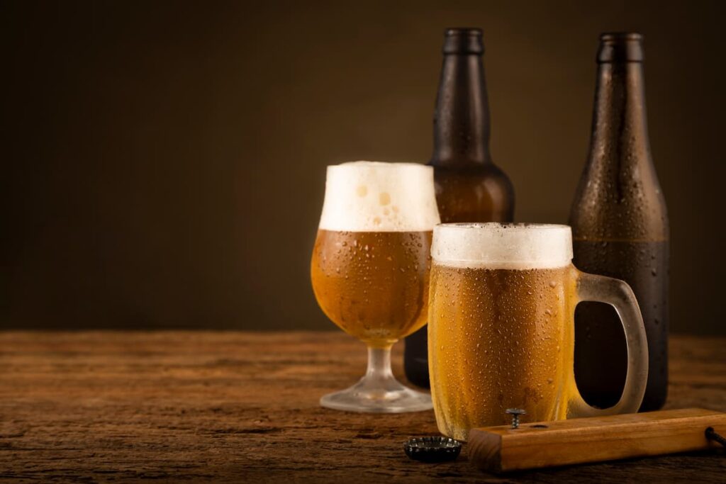 Dua garrafas de cerveja junto com dois copos de chopp em uma mesa de madeira