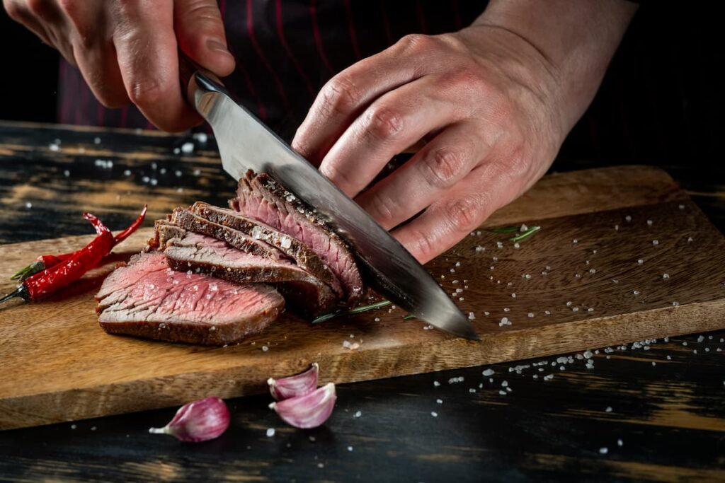 Uma pessoa cortando a carne em uma tábua de madeira