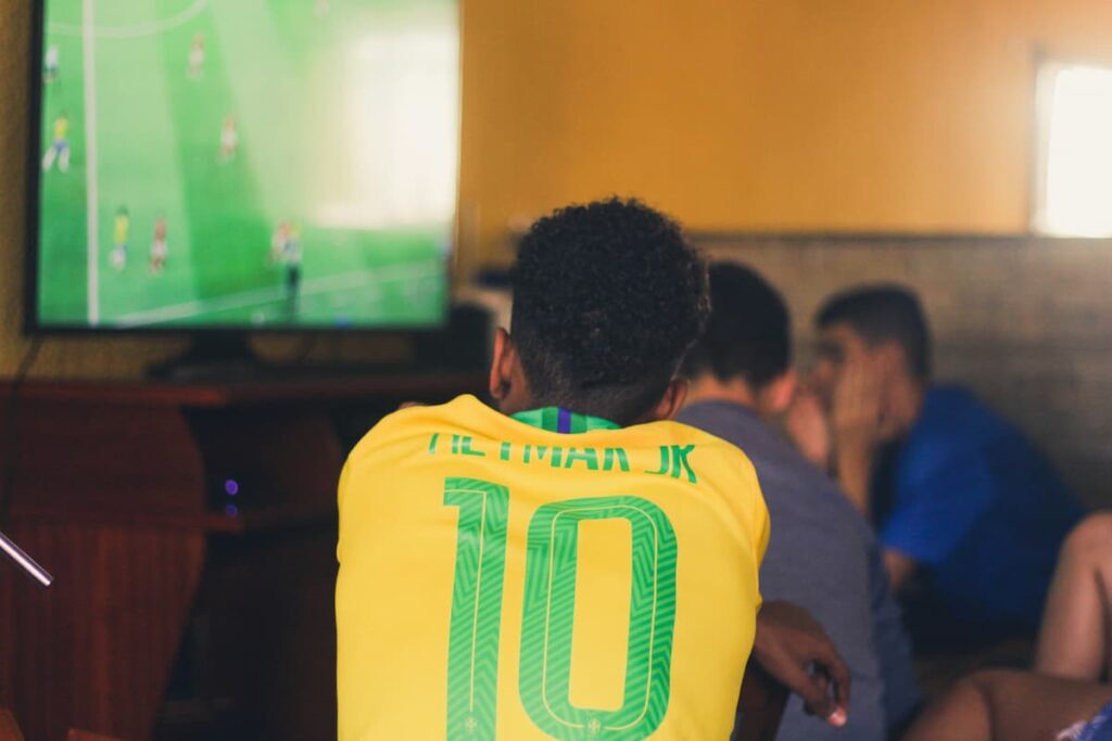 Menino com a camisa do Brasil, assistindo o jogo com seus amigos em casa
